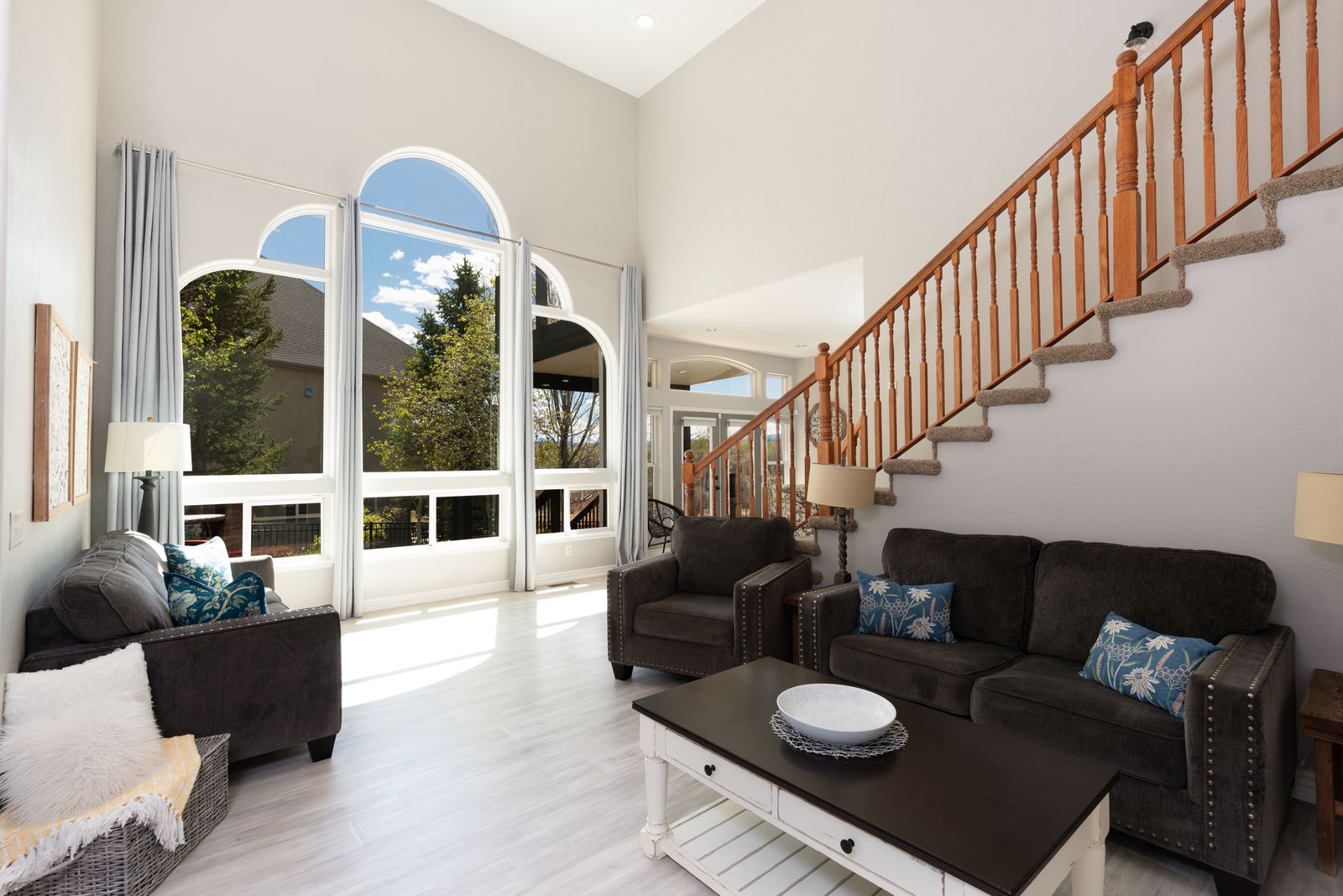 Living room with tall arched windows, staircase, and natural light flooding seating area