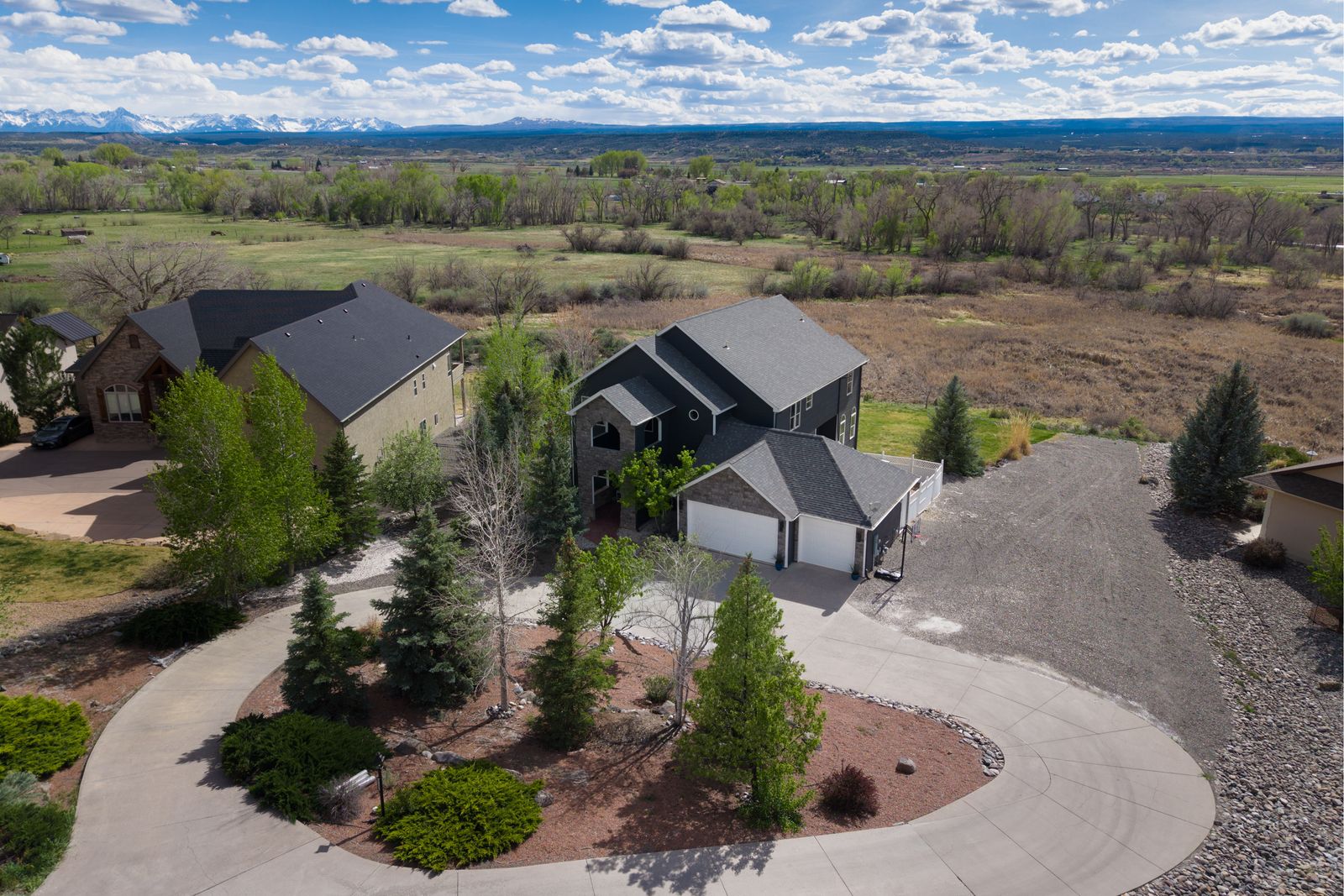 Aerial drone view of home on cul-de-sac with San Juan Mountains, green fields, and blue sky