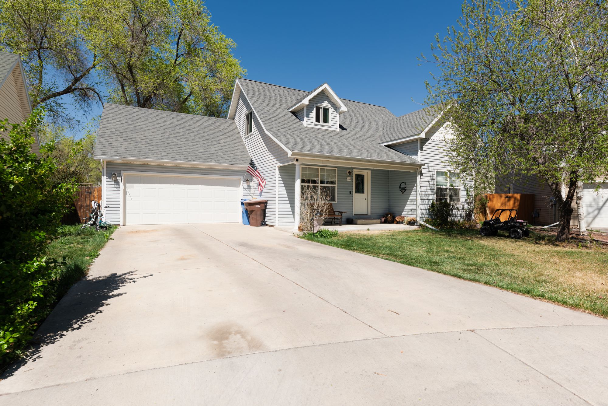 Front exterior of home with two-car garage, covered porch, and mature trees