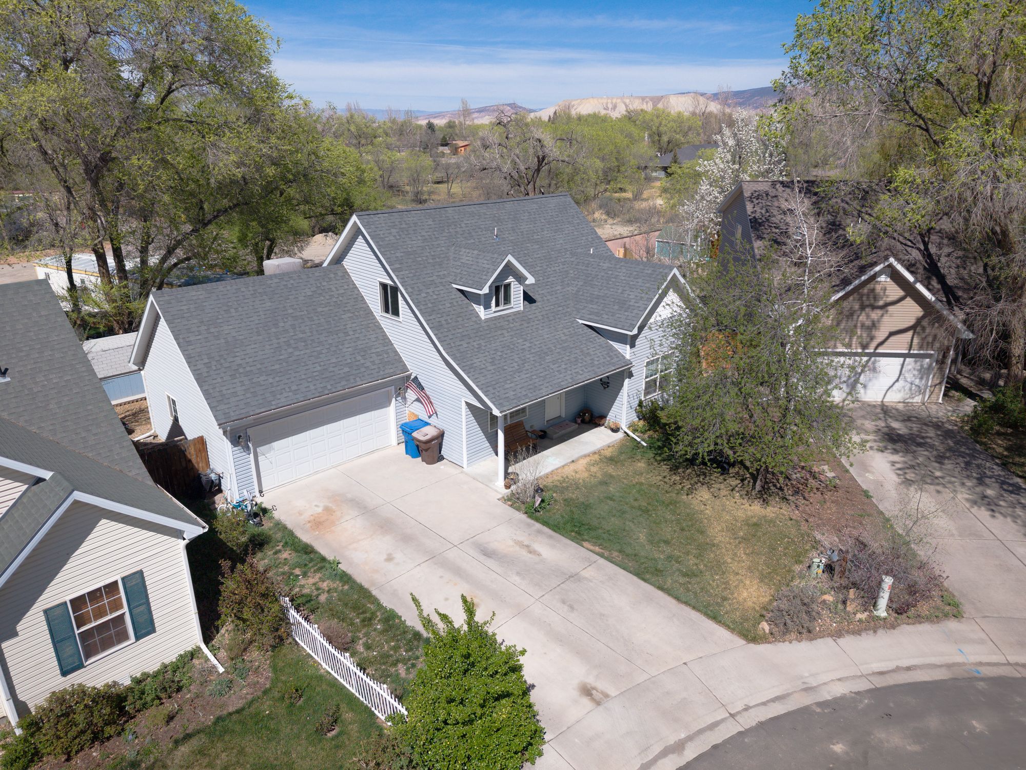 Aerial drone view of home showing roofline, yard, and neighborhood with mountain views