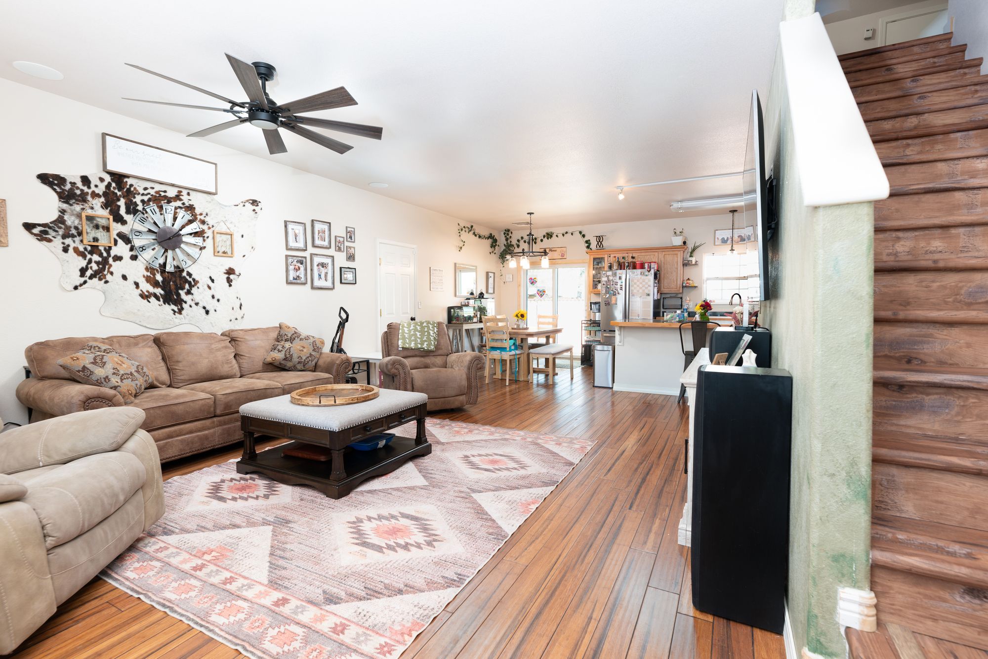Open-concept living room with hardwood floors, ceiling fan, and staircase