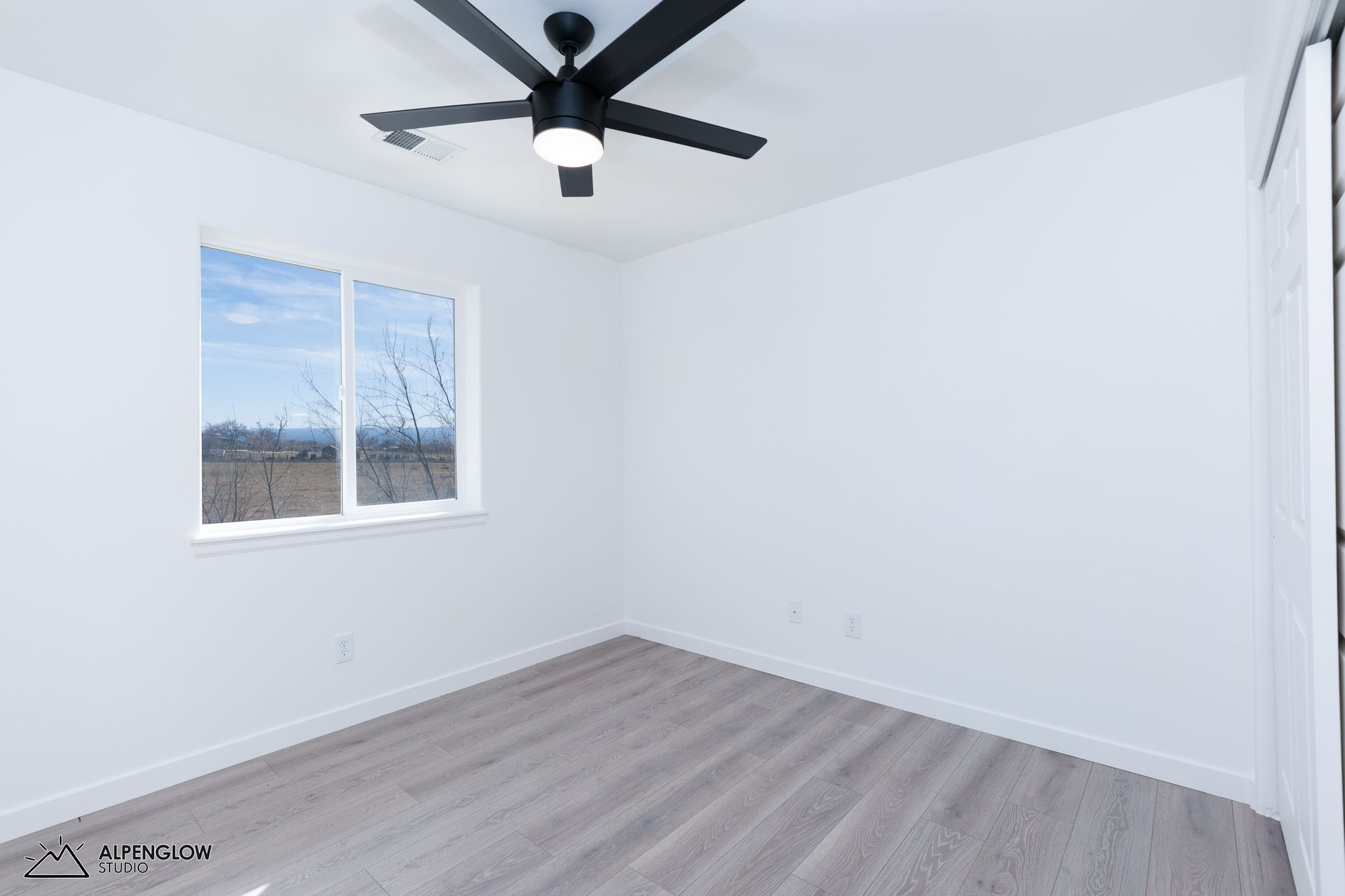 Guest bedroom with hardwood floors, ceiling fan, and window views